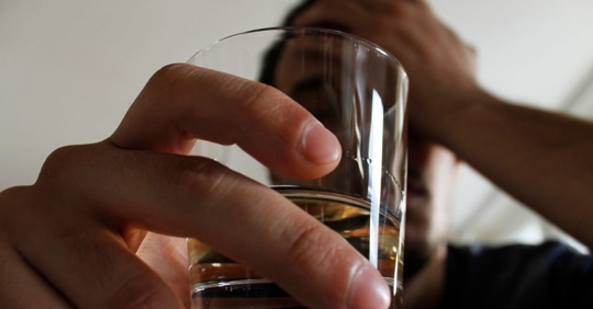 Individual holding an alcoholic shot in their hand, contemplating about their life choices